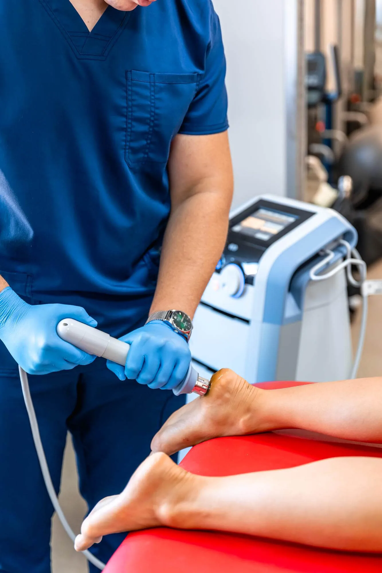 Chiropractor in blue scrubs using handheld laser therapy device on patient's leg.
