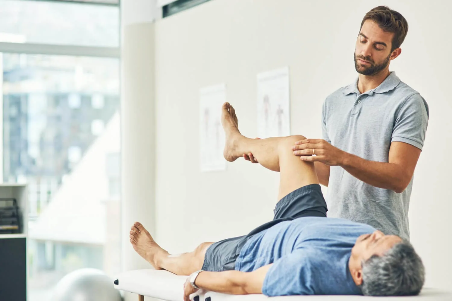Chiropractor examining patient's leg and knee during physical therapy session in bright clinic.